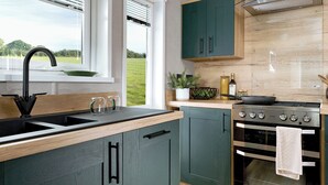 A modern kitchen with a sink, stove, and green cabinets. - Premium Holiday Home 3 bed HT Pet (Great Yarmouth)