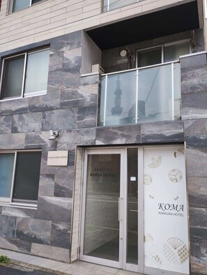 A modern building facade with stone cladding, a glass entrance door, and a sign for Asakusa Koma Hotel. - 6 minutes walk from Asakusa Sta. (Sumida City)