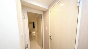 Un couloir avec une porte fermée, un interrupteur et un luminaire fixé au mur.