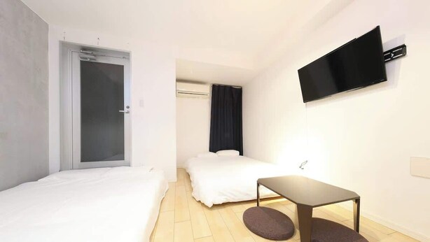 Une chambre d’hôtel avec un lit, une petite table, un téléviseur fixé au mur et une porte.