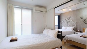 Een slaapkamer met twee bedden, een raam met gordijnen, een airconditioner en een metalen bedframe.