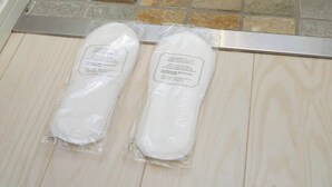 Un par de zapatillas blancas con etiquetas sobre un suelo de madera, con una pared de piedra al fondo.