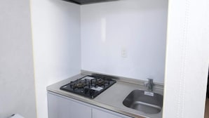 Una cocina compacta con estufa a gas, pileta de acero inoxidable y campana extractora instalada en la pared.