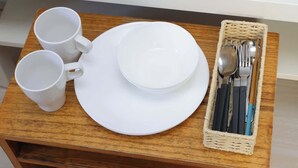 Una mesa de madera con tazas blancas, un plato y una cesta con cubiertos.