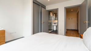 Una camera da letto con un letto, una cassettiera in legno, un bagno con doccia in vetro e un corridoio che conduce a un'altra stanza.