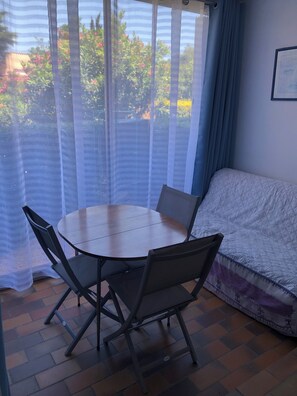 A room with a round table and four chairs, a sofa, and a window with sheer curtains. - T2 with pool, private parking, walking distance to the beach - 4 pers - ARGELES SUR MER (Argelès-sur-Mer)