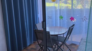 A room with a glass door, a table with chairs, and a view of trees through the door. - T2 with pool, private parking, walking distance to the beach - 4 pers - ARGELES SUR MER (Argelès-sur-Mer)