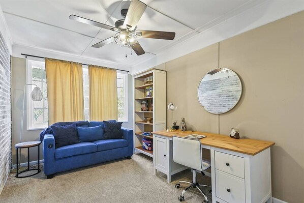 A room with a blue sofa, a desk with drawers, a round mirror, and a ceiling fan. - 3BR Home Near Savannah | Pet-Friendly Stay (Savannah)