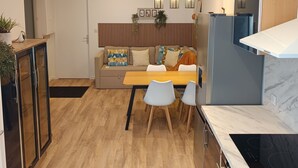 Una cocina moderna con estufa integrada, un comedor con mesa y sillas de madera, y una zona de estar con sofá y cojines decorativos.