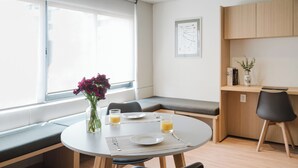 A modern dining area with a round table, bench seating, a vase with flowers, and a window with a view. - Modern 1BR in Juárez with fast WiFi, great natural light, a comfortable king bed, a fully equipped kitchen, and a luxury bathroom. Perfect for couples or solo travelers seeking comfort, style, and a prime location in Mexico City. (Cuauhtémoc)