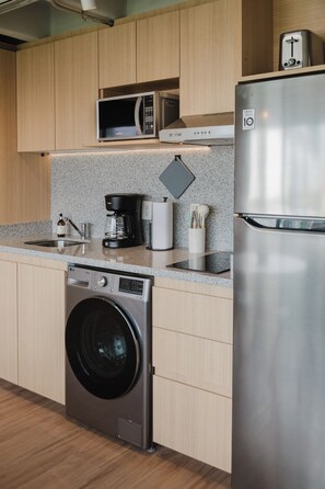 A modern kitchen with wooden cabinets, a stainless steel washing machine, a microwave, a coffee maker, and a refrigerator. - Modern 1BR in Juárez with fast WiFi, great natural light, a comfortable king bed, a fully equipped kitchen, and a luxury bathroom. Perfect for couples or solo travelers seeking comfort, style, and a prime location in Mexico City. (Cuauhtémoc)