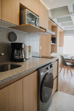 A modern kitchen with wooden cabinets, a built-in washing machine, a coffee maker, and a microwave. - Modern 1BR in Juárez with fast WiFi, great natural light, a comfortable king bed, a fully equipped kitchen, and a luxury bathroom. Perfect for couples or solo travelers seeking comfort, style, and a prime location in Mexico City. (Cuauhtémoc)