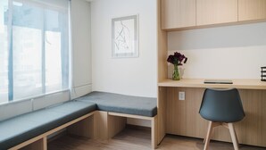 Ein Zimmer mit einer Bank, einem Schreibtisch, einem Stuhl, einer Vase mit Blumen und einem gerahmten Bild an der Wand.