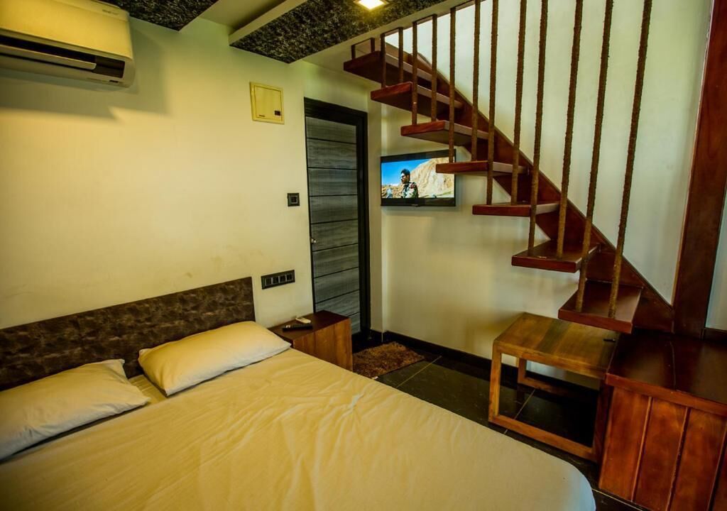A bedroom with a bed, a wooden staircase, a TV, and an air conditioning unit.