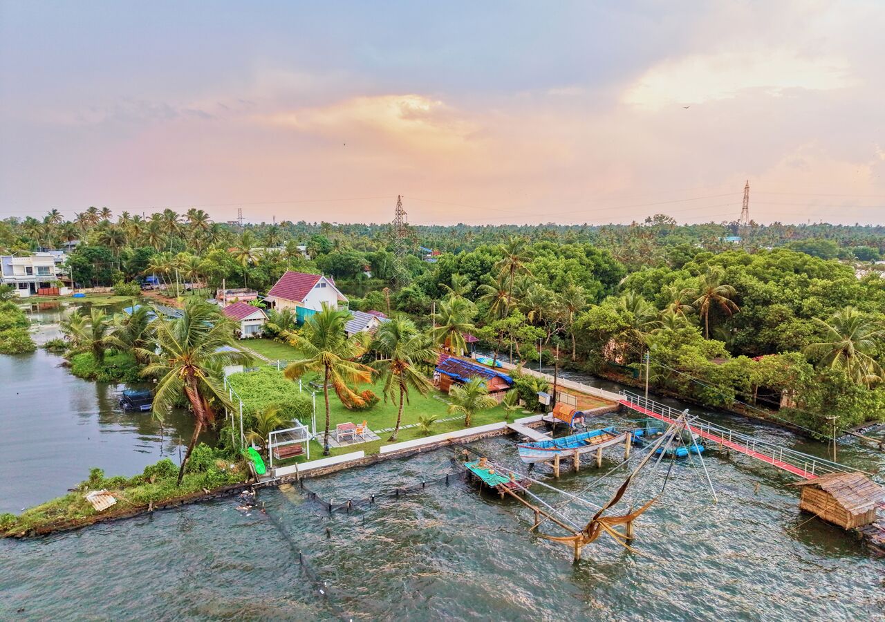 Un pueblo a orillas del río con barcos, un puente de madera y casas rodeadas de vegetación.