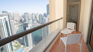 A balcony with a glass railing overlooking a cityscape with high-rise buildings and a body of water. - GMA Amwaj 2BR Sea View High Floor (Dubai)