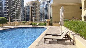 A swimming pool with lounge chairs, a sun umbrella, and high-rise buildings in the background. - GMA Amwaj 2BR Sea View High Floor (Dubai)