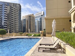 Ein Pool mit Liegestühlen, Sonnenschirm und Hochhäusern im Hintergrund.