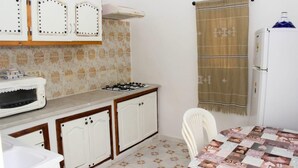Una cocina compacta con estufa a gas, armarios blancos, un refrigerador y un mantel estampado.