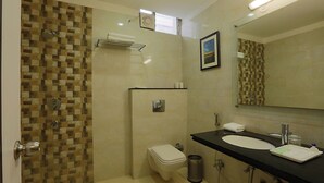 Un baño con pared de ducha en cerámica, inodoro, lavamanos con espejo y un cubo de basura.