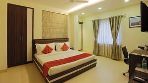 Habitación de hotel con cama, escritorio, silla, televisión y ventilador de techo.
