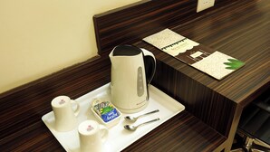 Habitación de hotel con un escritorio de madera, una bandeja blanca con cafetera, dos tazas, una caja de pañuelos y una cuchara.