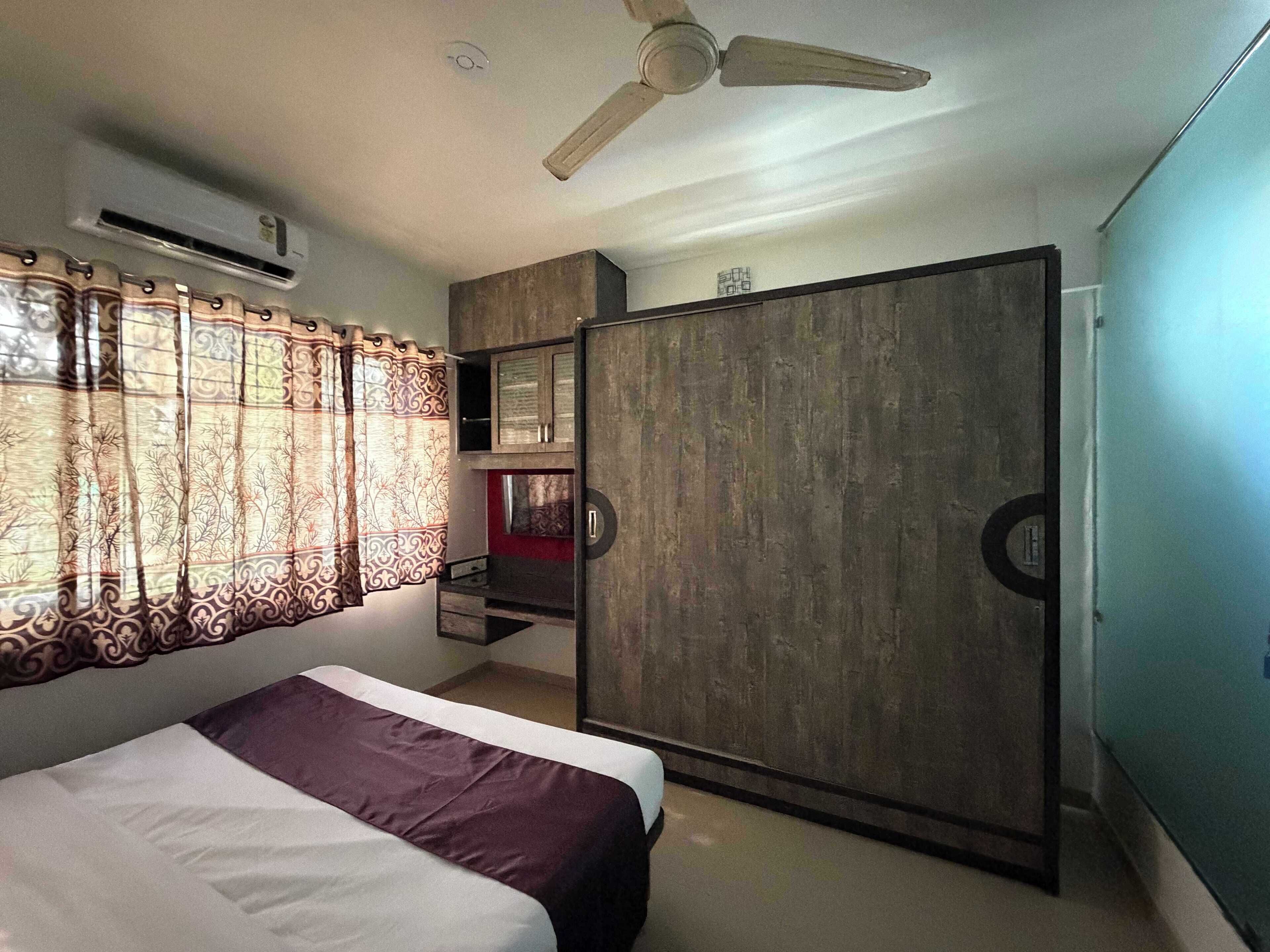 A bedroom with a bed, a wardrobe, a ceiling fan, and an air conditioning unit.
