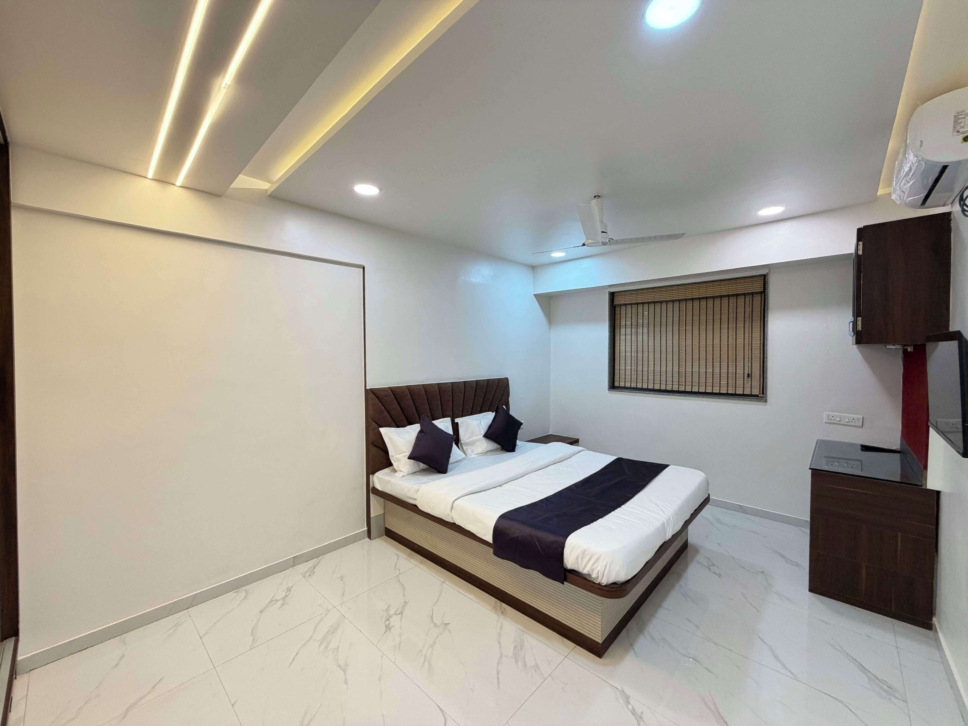 A modern bedroom with a bed, a ceiling fan, a window with blinds, and a built-in TV.