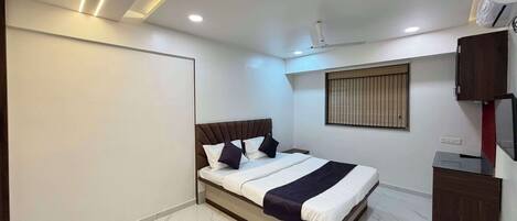 A modern bedroom with a bed, a ceiling fan, a window with blinds, and a built-in TV.