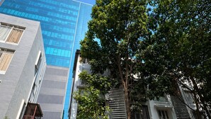 Un edificio moderno con fachada de vidrio, entrada arbolada y una scooter estacionada.