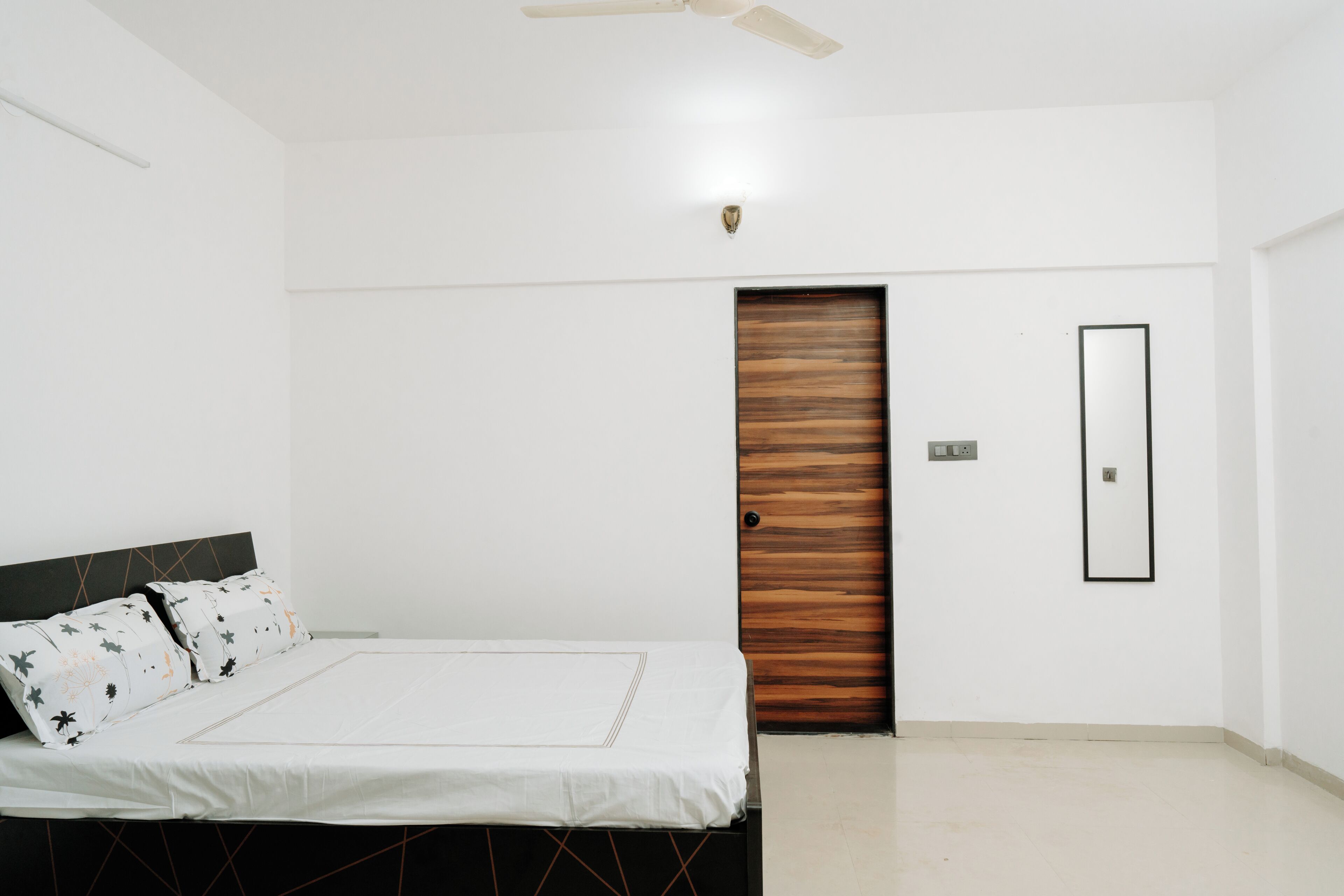 Un dormitorio con cama, una puerta de madera, un espejo y un ventilador de techo.