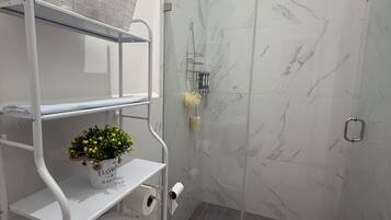 Et badeværelse med toilet, bruser med glasdør og en hylde med en potteplante.