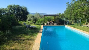 Une piscine avec des chaises longues et un espace salon abrité.