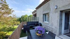 A patio with outdoor furniture, a table with a flower vase, and a view of a house with a window and a door. - Air-conditioned apartment surrounded by vineyards, with a shared pool   (La Tour-d'Aigues)
