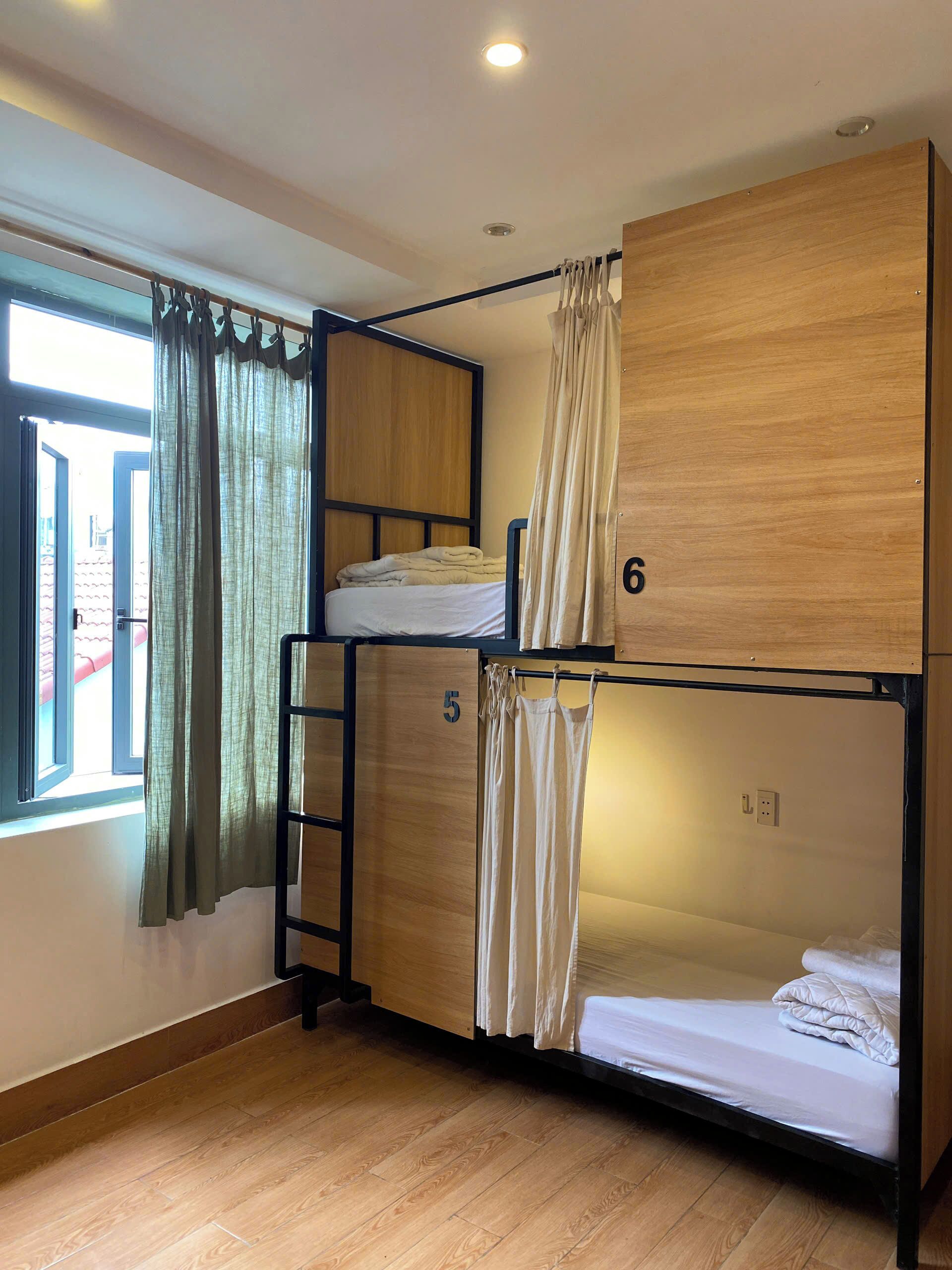 Une chambre de dortoir avec des lits superposés, des lits numérotés, une fenêtre avec des rideaux et un plancher en bois.