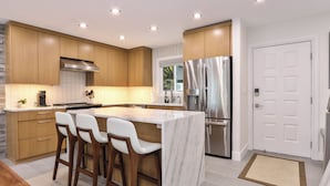 A modern kitchen with wooden cabinets, a stainless steel refrigerator, and a marble island with bar stools. - Ski in/out @ Camelback: Sleeps up to 16 (Tannersville)