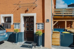 Un edificio con fachada marrón texturizada, una puerta de madera con paneles de vidrio y dos macetas grandes con plantas.