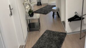 A hallway with a wooden floor, a grey rug, a small table with a plant, and a mirror on the wall.