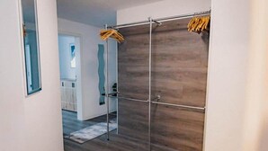 Un couloir avec un plancher en bois, un portant en métal où sont suspendus des vêtements et un miroir accroché au mur.