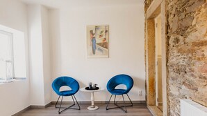 Une pièce avec deux chaises bleues, une petite table sur laquelle se trouve un vase, et un tableau accroché au mur.