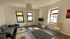A modern living room with a sofa, coffee table, TV, and a view of the outside. - Fewos4seasons vacation apartment 7 (Oberwiesenthal)