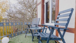 Een balkon met twee blauwe stoelen en een glazen tafel, omgeven door een metalen hekwerk.