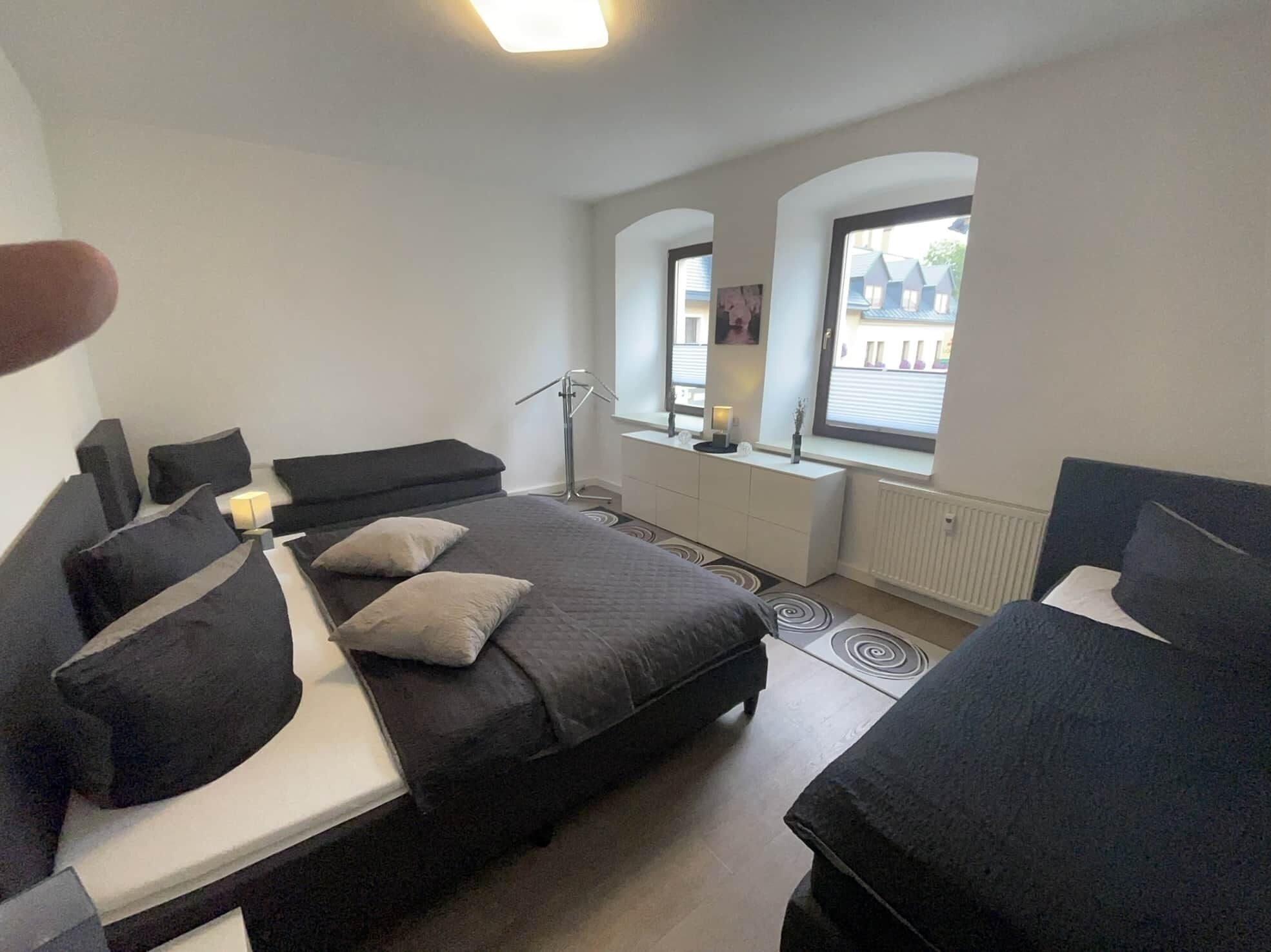 Une chambre à coucher avec un lit, des tables de chevet, une lampe, une fenêtre et un radiateur.