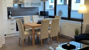 Een moderne keuken met witte kasten, een houten eettafel en stoelen. Er is een glazen salontafel en een lamp op een bijzettafeltje.