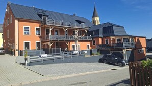 Een meerhoog gebouw met een kerktoren, een parkeerplaats en een hekwerk.