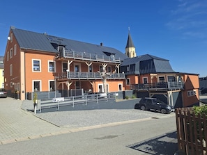 Un edificio de varios pisos con una aguja de iglesia, un estacionamiento y una entrada con portón.