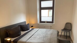 A bedroom with a bed, bedside lamps, a chair, a window, and a radiator. - Fewos4seasons vacation apartment 6 (Oberwiesenthal)