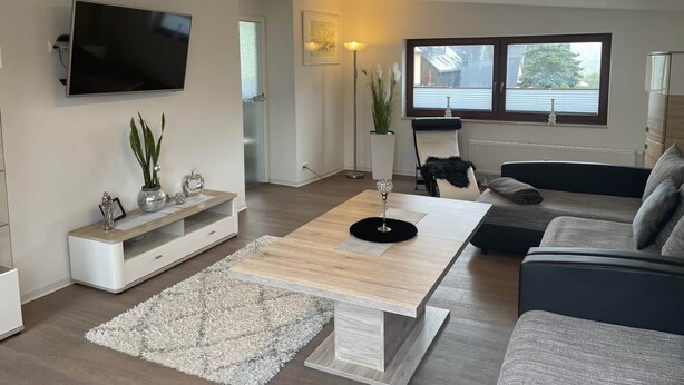 Una sala de estar moderna con un televisor de pantalla plana, una mesa de centro de madera, un sofá y un ventanal grande.