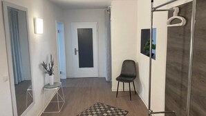 Un pasillo con alfombra a cuadros, una silla, una planta en maceta, una puerta y un espejo.