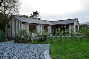 A wooden house with a sloped roof, a gravel driveway, and a grassy lawn with small plants. - Private Lodge With Hot tub in Blackpool (Blackpool)